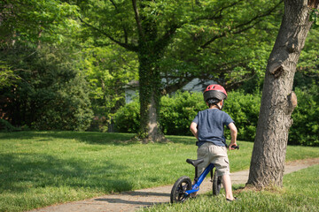 Young boy preparing to ride balance bike on suburban sidewalk.