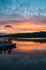 Obraz premium Two adirondack chairs on end of dock on lake at sunrise.