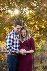 Fototapeta premium Expecting couple embracing, hands on mother's belly, fall backdrop