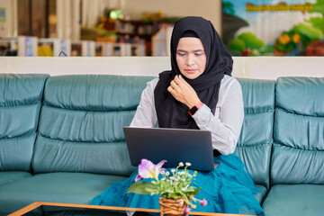 Asian muslim woman in hijab using laptop in office