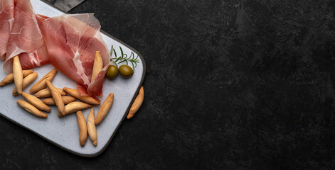 Flat lay with Spanish jamon and picos - bread sticks on dark table and grey desk, copy space. Snack from Spain concept - obrazy, fototapety, plakaty
