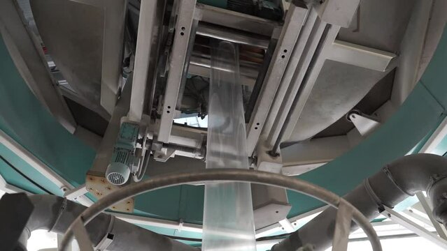 The operation of automatic plastic bag production machine.  Natural color LDPE single layer Shrink film by old technology extrusion blown film plastic bag making machine.