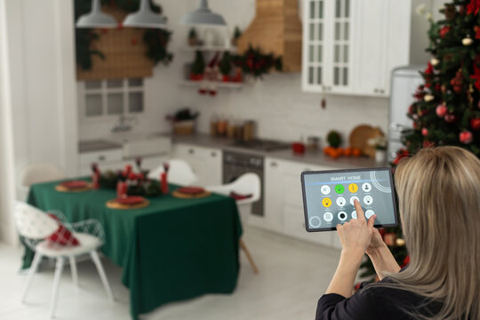 Woman pushing button on kitchen app of smart home on digital tablet at home. Concept of modern home control. Idea of domestic lifestyle. Cropped image of girl. Blurred man on background using laptop.
