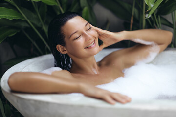 Portrait of multiracial Caucasian Asian girl taking bath in a stylish concrete bathtub. Amazing...