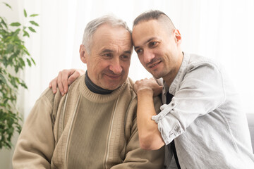 Happy two generations male family old senior mature father and smiling young adult grown son enjoying talking chatting bonding relaxing having friendly positive conversation sit on sofa at home.