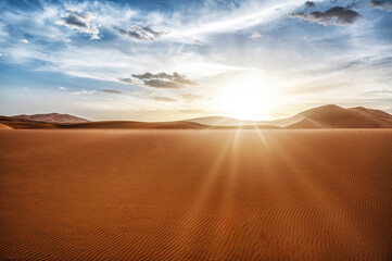 Desert dunes landscape with sun flare on cloudy sky background.