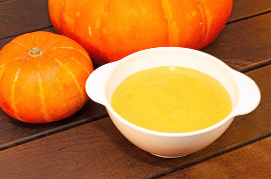Pumpkin hot soup puree and pumpkins on a wooden table