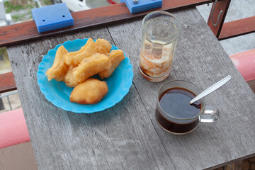 Patongko on a blue plastic plate Black coffee and poached eggs in a glass on a wooden table
