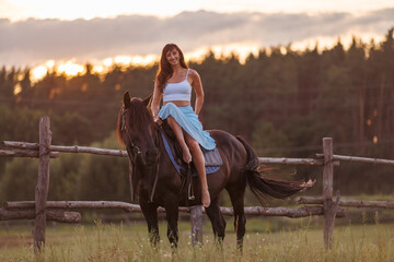 A young girl sits on a horse. Rider against the backdrop of the forest at sunset
