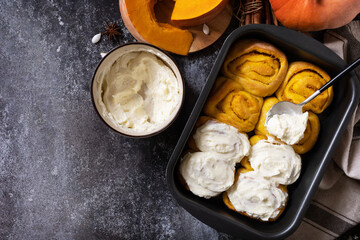 Freshly baked pumpkin cinnamon rolls or cinnabon with cream cheese on a dark stone background. Homemade seasonal autumn homemade pastry. View from above. Copy space.