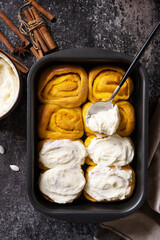 Homemade seasonal autumn homemade pastry. Freshly baked pumpkin cinnamon rolls or cinnabon with cream cheese on a dark stone background. View from above.