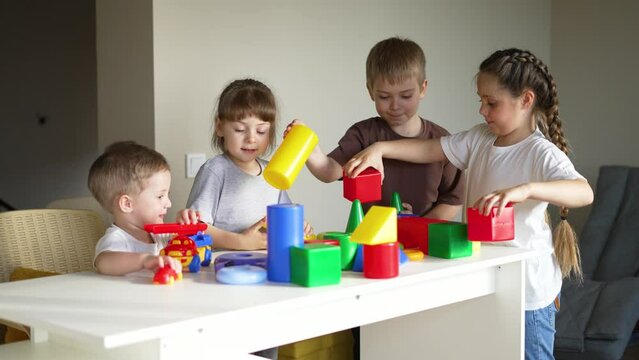 Children in kindergarten. Preschool education in games. Boys and girls play at table at home. Colored cubes and pyramid on table. Child care in kindergarten. Children play and dream. Toy car in hands