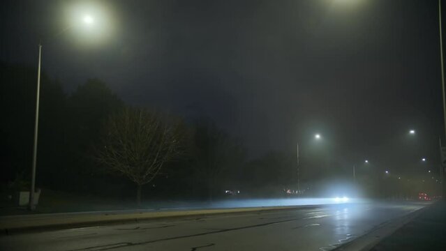 Cars drive on road of smoke and fog at night time. Wide shot