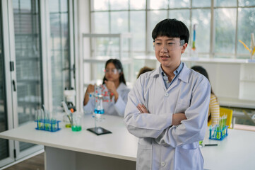 Asian boy student learning and doing chemical experiment in science class. Cute teenager male standing and smiling while learning chemistry class in laboratory room.
