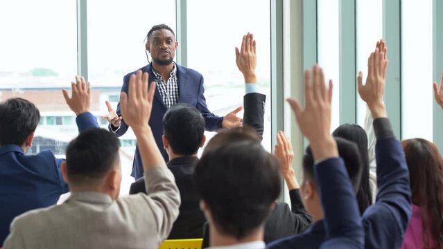 african american business man standing and talking in font of group of diversity business people in meeting at seminar listener raising hand to ask question. black speaker giving lecture