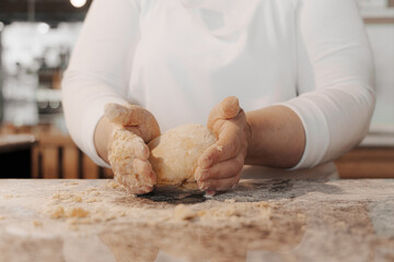 Crop anonymous female cook in white uniform kneading dough making ball on marble counter in restaurant kitchen