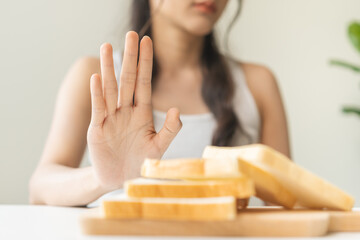 Gluten allergy, asian young woman hand push out, refusing to eat white bread slice on chopping board in food meal at home, girl having a stomach ache. Gluten intolerant and Gluten free diet concept.