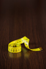 A tailor's measuring tape of yellow color lies on a dark wooden table. Selective voicing. Place for text. Copyspace.