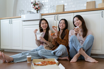 Beautiful group of Asian friends wearing sweater sits on the floor enjoy eating pizza and takeaway...