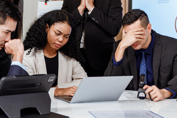 A team of business men and women look at the computer showing their stress over not achieving their...