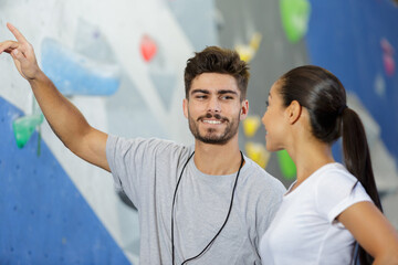 happy man and woman talking at indoor climbing gym wall - obrazy, fototapety, plakaty