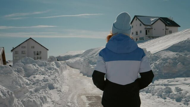 Caucasian woman walking on snow towards winter ski logde. Tourist female coming back to the chalet after morning walk.