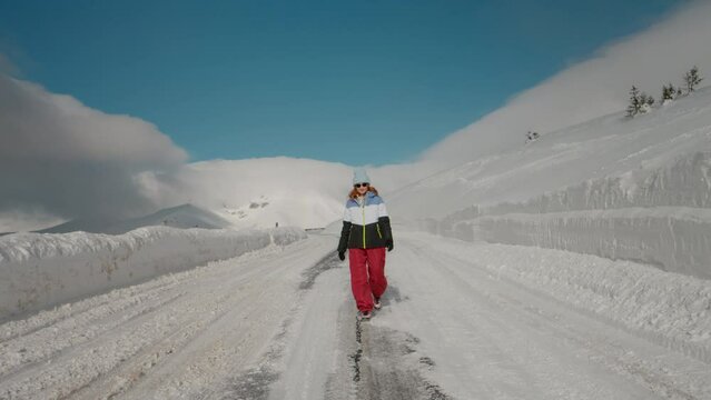Huge snowfall during winter in the mountains and woman walking on snow cleaned road. Advertising warm termal winter clothes.