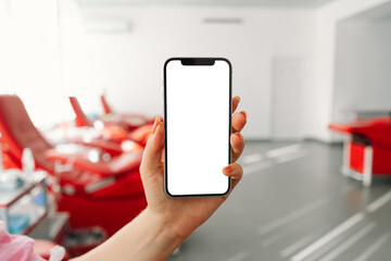 Blood donation. Close up of female hand holding smartphone with blank screen at blood donation center. Copy space