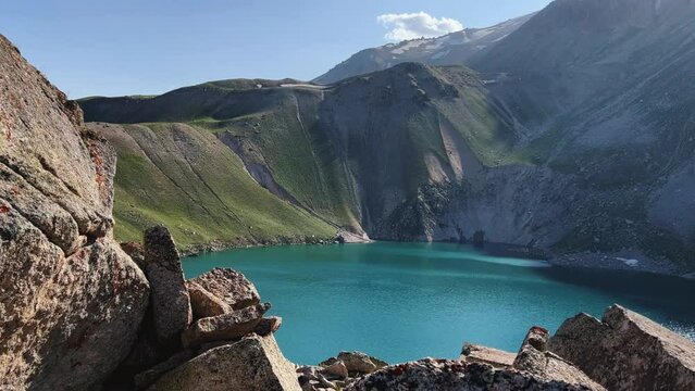 Turquoise mountain lake on the high plateau of Angren. View from the top of the mountain to the large lake Arashan at an altitude of 3365 m above sea level. Blue sky over the lake. Uzbekistan 4K
