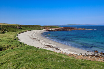 Fototapeta na wymiar Blue water white sand scottish beach in scotland with grass and dunes