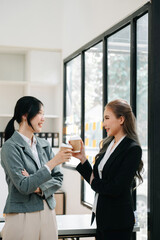 Happy two Asian business woman holding coffee cup in coworking office..