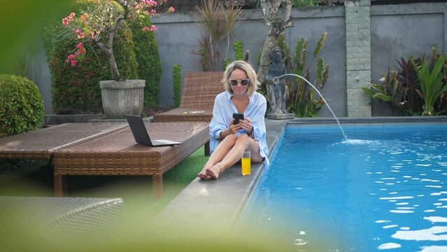 Mid adult woman calling on phone near the swimming pool at sunset time