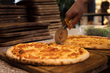 Close up of anonimous pizza chef slicing appetising pizza with cutter wheel in order to be served...