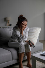 Fototapeta premium Asian woman sitting on sofa holding phone feeling disappointed, sad, upset. Female suffer from mental health problems.