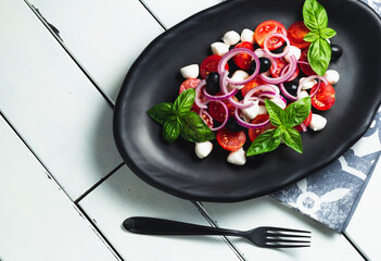 Italian cuisine. Fresh Italian Caprese salad with mozzarella and tomatoes on dark plate on white wooden table. Top view