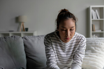 Lonely Asian woman in distress, worried, confused, sitting on sofa at home. Female suffer from mental health problems.