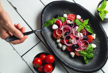 Tomato and mozzarella Caprese salad and pesto sauce with olives on white table served with fork....