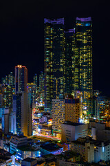 Naklejka premium Busan City skyline, skyscrapers, and modern buildings at night, illuminated in vibrant colors over the Haeundae Beach in Kyongsang Namdo, South Korea