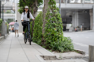 Fototapeta premium Eco friendly vehicle. 20s businesswoman ride bicycle to work in urban. Cycling is carbon neutral, transport to global warming. Environment preservation by sustainable energy commuting with bicycling