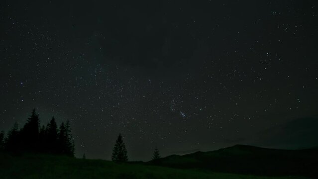 Time lapse of moving clouds and stars over the mountains in the night sky