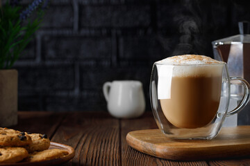 cappuccino in cup and geyser coffee maker on wooden table with black brick wall as background