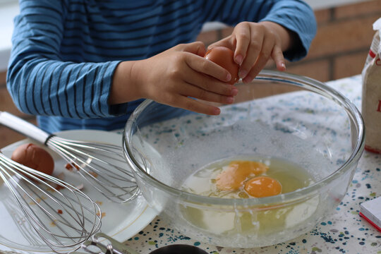 Child broke fresh egg. Child hand cracking egg for cooking, baking cake, waffles at home in the kitchen. Fresh free range eggs in a glass bowl.  Close up photo family lifestyle. 