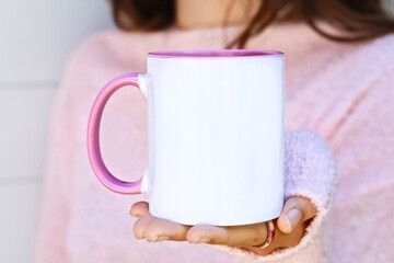 Girl is holding  blank pink handle white mug in hands and soft pink sweater. Blank 11 oz ceramic cup