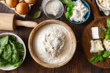 Set of raw ingredients for cooking Italian ravioli with various cheeses and spinach on a wooden table top view