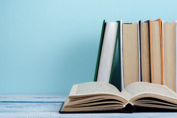 Book stacking. Open book, hardback books on wooden table and blue background. Back to school. Copy space for text.