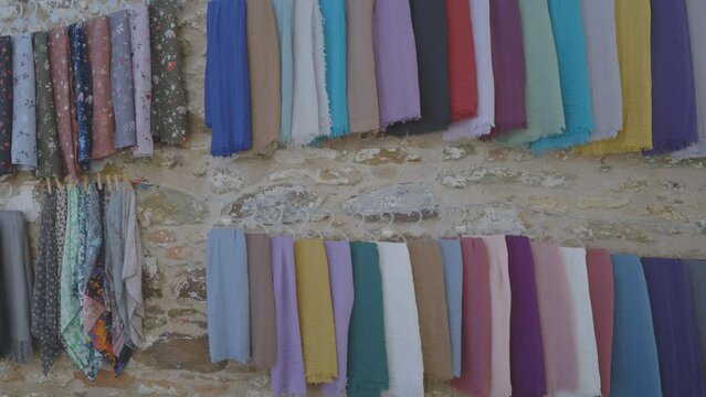 Traditional patterned shawls and fabrics on market in sea island village. Headscarves hanging on stone wall on sale market for tourists