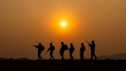 Fototapeta na wymiar silhouette group of special forces sodiers walking and holding gun over the sunset and colorful orange sky background,