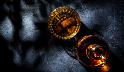 Whiskey, scotch or bourbon in glass and bottle, black stone background with hard light, shadows and sun glare, copy space