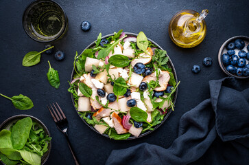 Fresh salad with sweet melon, grilled chicken breast, onion,  feta cheese, blueberries and mixed herbs, black table background, top view