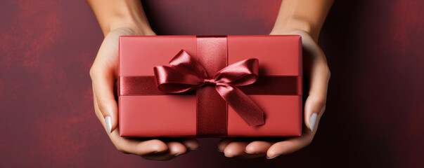 Female hands holding a gift box with a red bow on a red background - obrazy, fototapety, plakaty